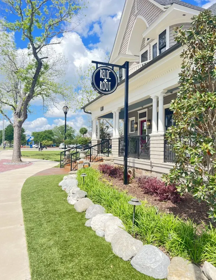 Restaurant exterior with sign; grass and stone landscaping, sidewalk, and blue sky.
