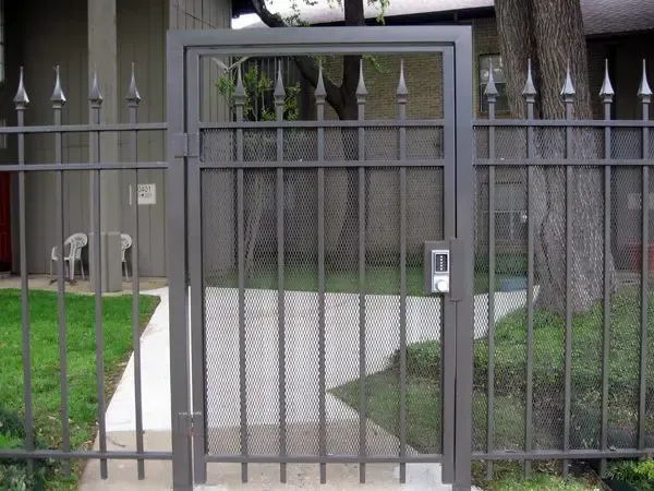 A gray metal gate in front of a concrete pathway. Spiked fence to the sides and behind.