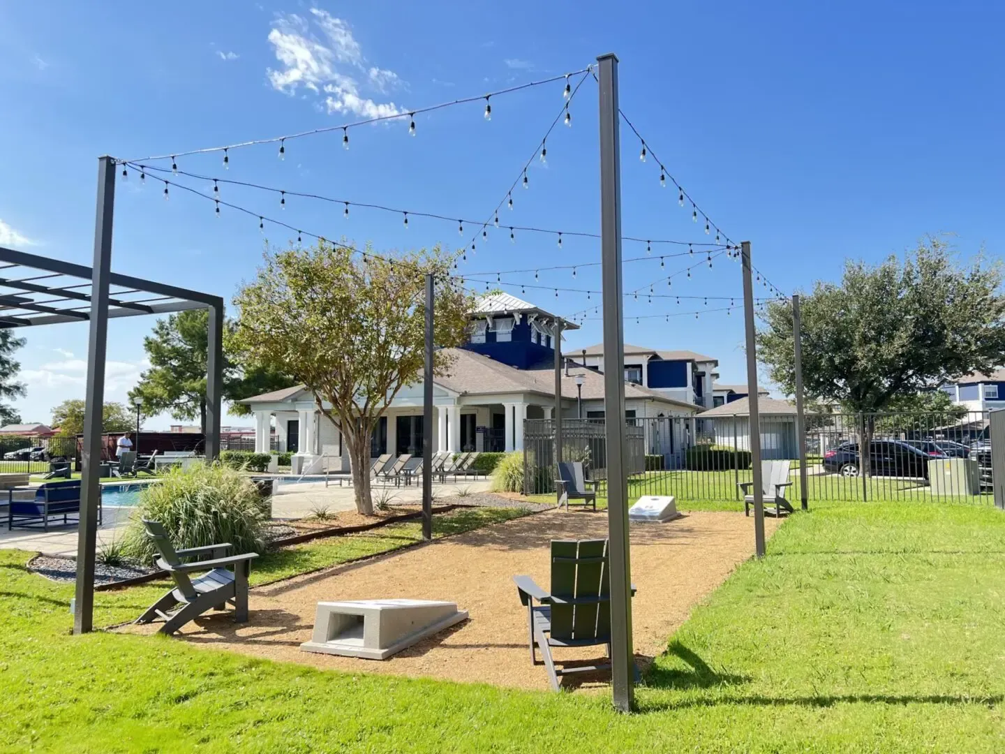 Outdoor seating area with string lights, a fire pit, chairs, and a building in the background.