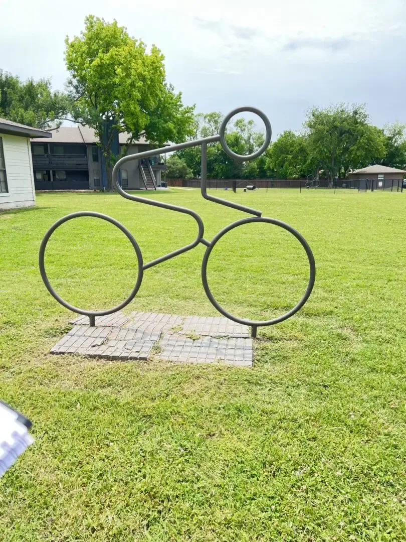 Metal sculpture of a cyclist in a grassy park.