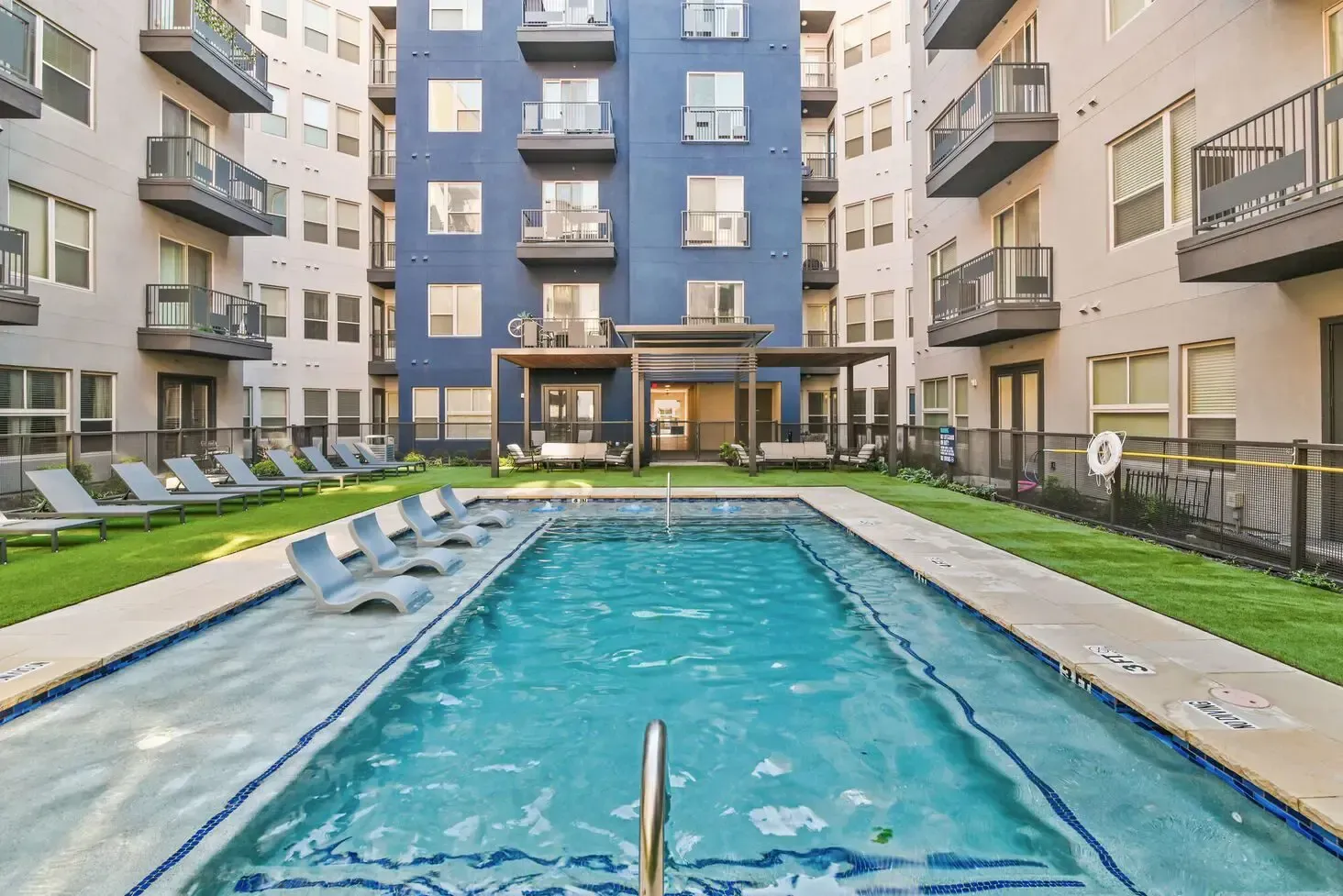 Swimming pool between apartment buildings with lounge chairs on the grass.