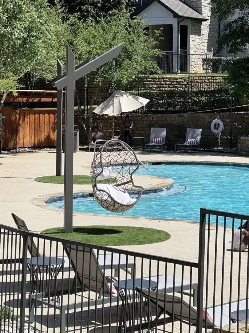 Poolside swing chair with a pool, fence, and loungers in the background.