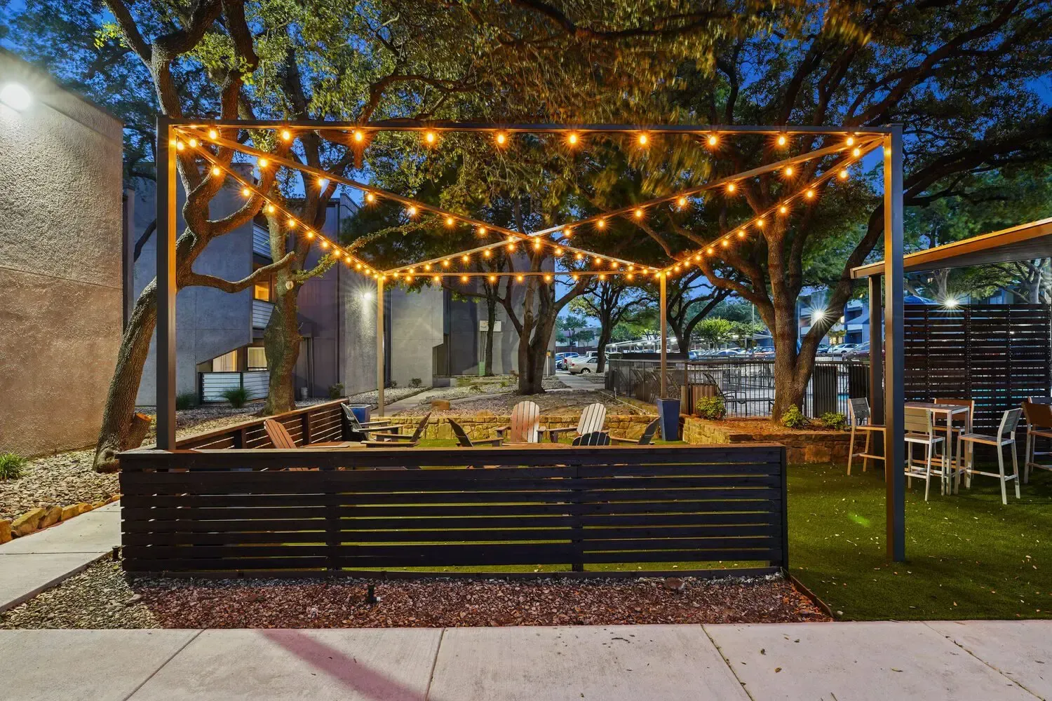 Outdoor patio with string lights, dark fence, and seating at dusk.
