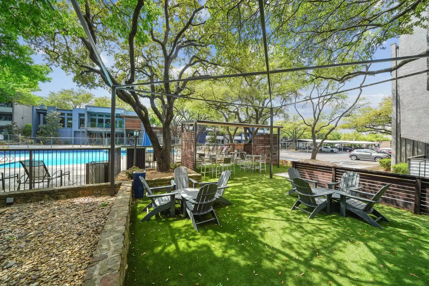 Outdoor patio with green turf, chairs, tables, near a pool and trees.