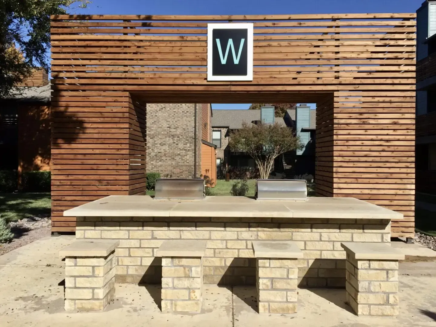 Wooden outdoor seating area with a “W” sign, a brick base, and horizontal wood panels.
