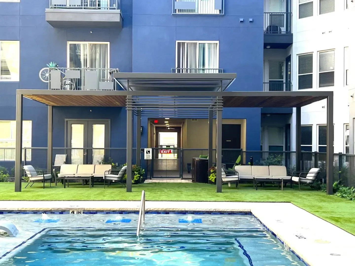 Pool area with blue building, metal pergola, seating, and a small pool.