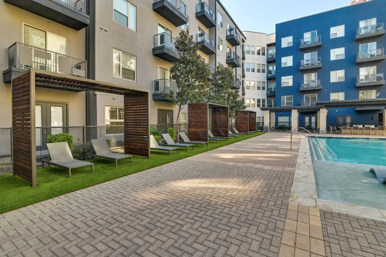Apartment complex courtyard with pool, lounge chairs, and wooden shade structures.