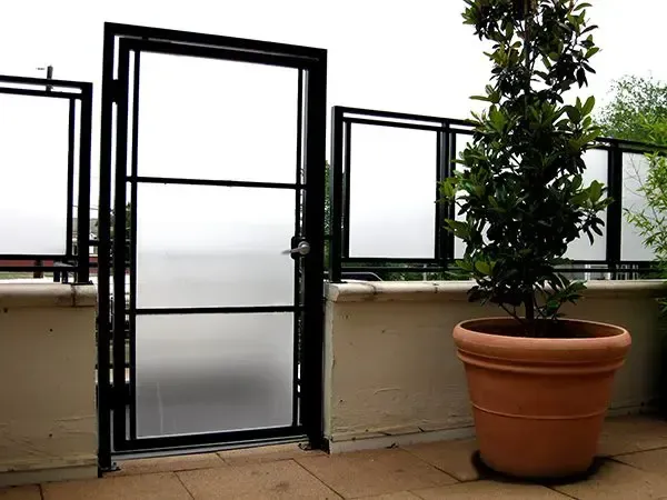 Black metal gate and railing with frosted glass panels on a patio, beside a potted plant.