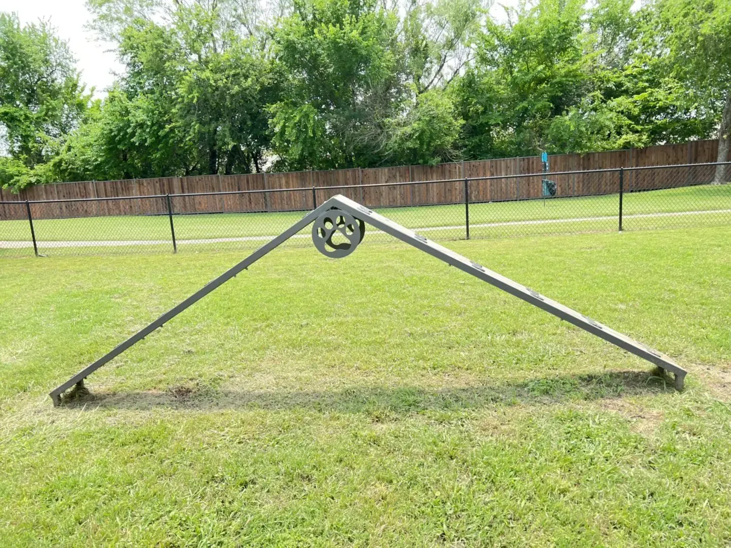 Gray dog agility A-frame in a grassy dog park with trees.