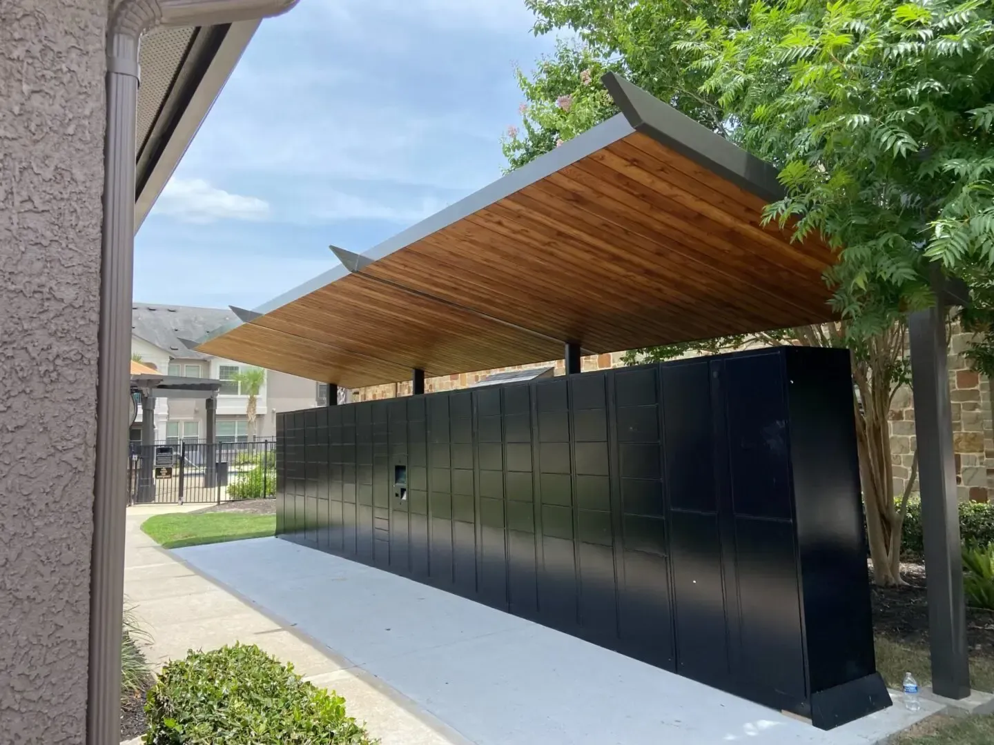 Black mailboxes under a wooden awning; a sidewalk and landscaping are visible.
