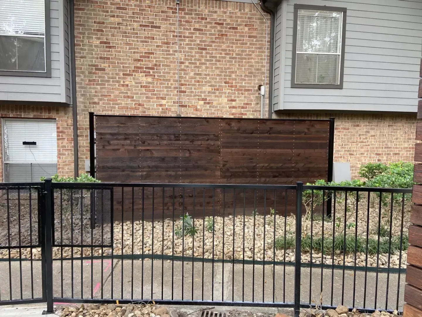 A brown wooden privacy fence between a black metal fence and a brick building.