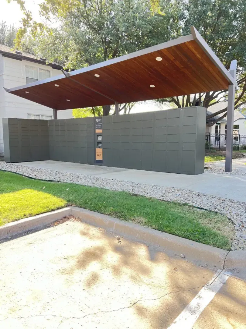 Modern carport with wooden roof and green wall. Gravel and grass surrounding.