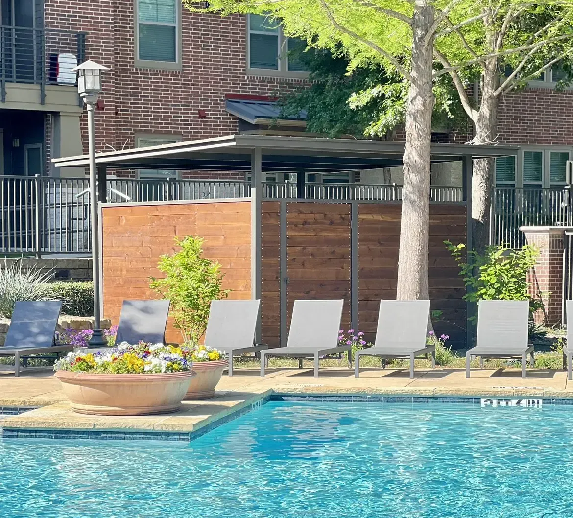 Poolside seating area with lounge chairs, trees, and wooden privacy screens.