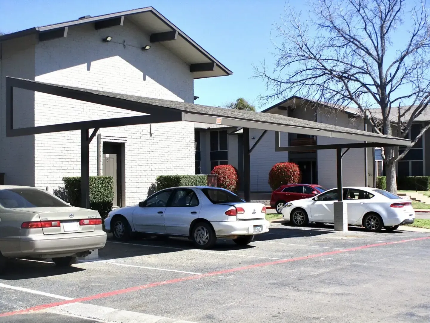Cars parked under a carport in front of a two-story apartment building.