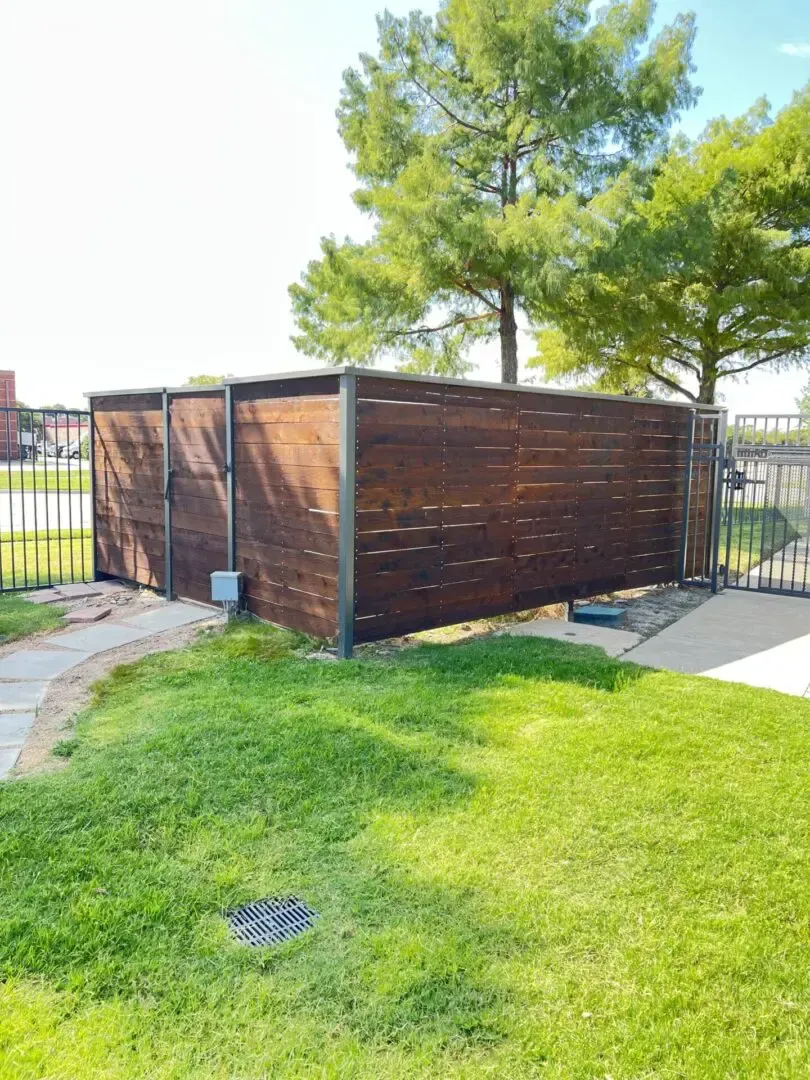 Wooden fence encloses an area with a gate. Green grass in the foreground. Bright day.