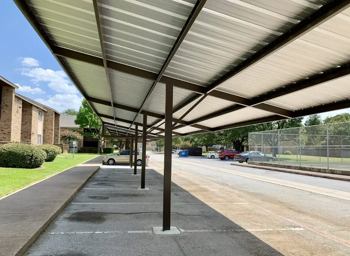 A row of covered parking spaces with metal roofs. Cars parked beneath a steel frame structure.
