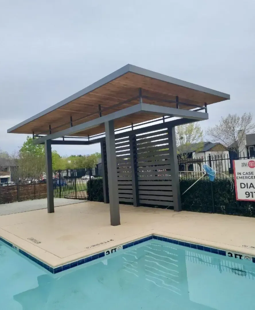 Poolside pergola with gray metal frame, wooden roof, and slatted side panels.