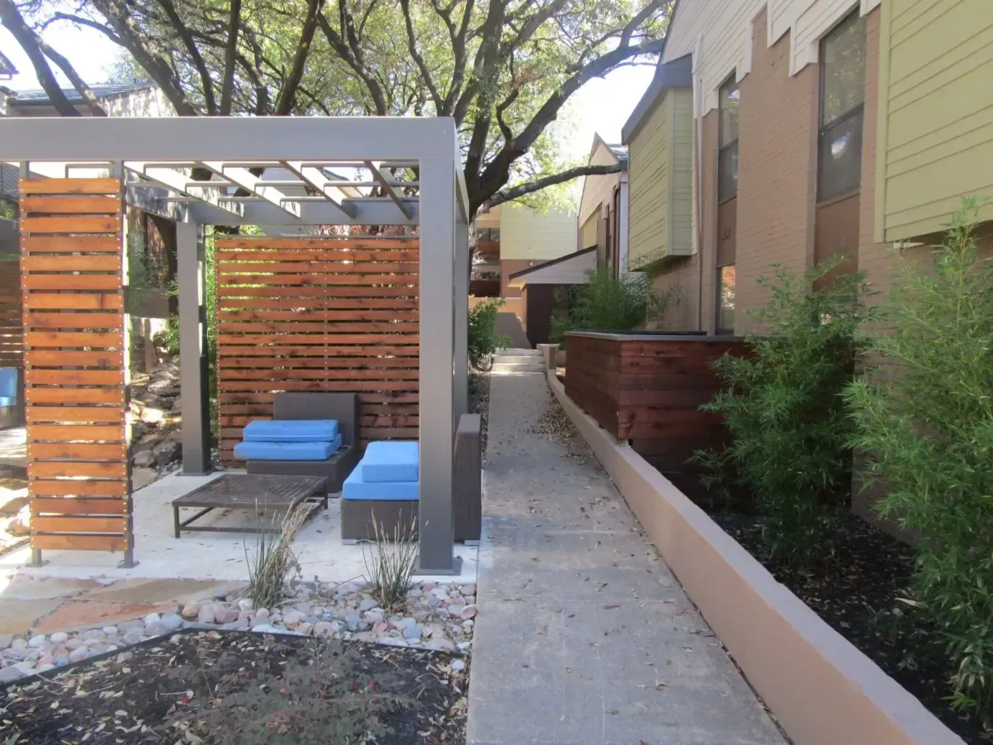 Outdoor lounge area with seating, wooden screens, and a walkway beside a building.