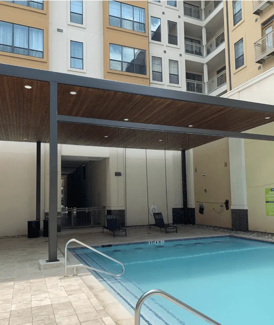 Pool with a shaded seating area. Light tan building in background.