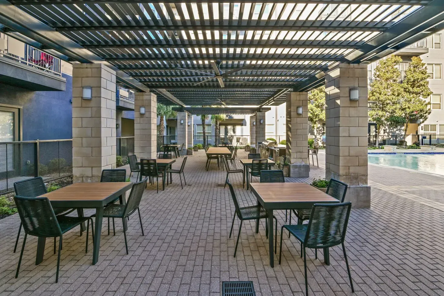 Outdoor dining area with tables, chairs, and pergola near a swimming pool.
