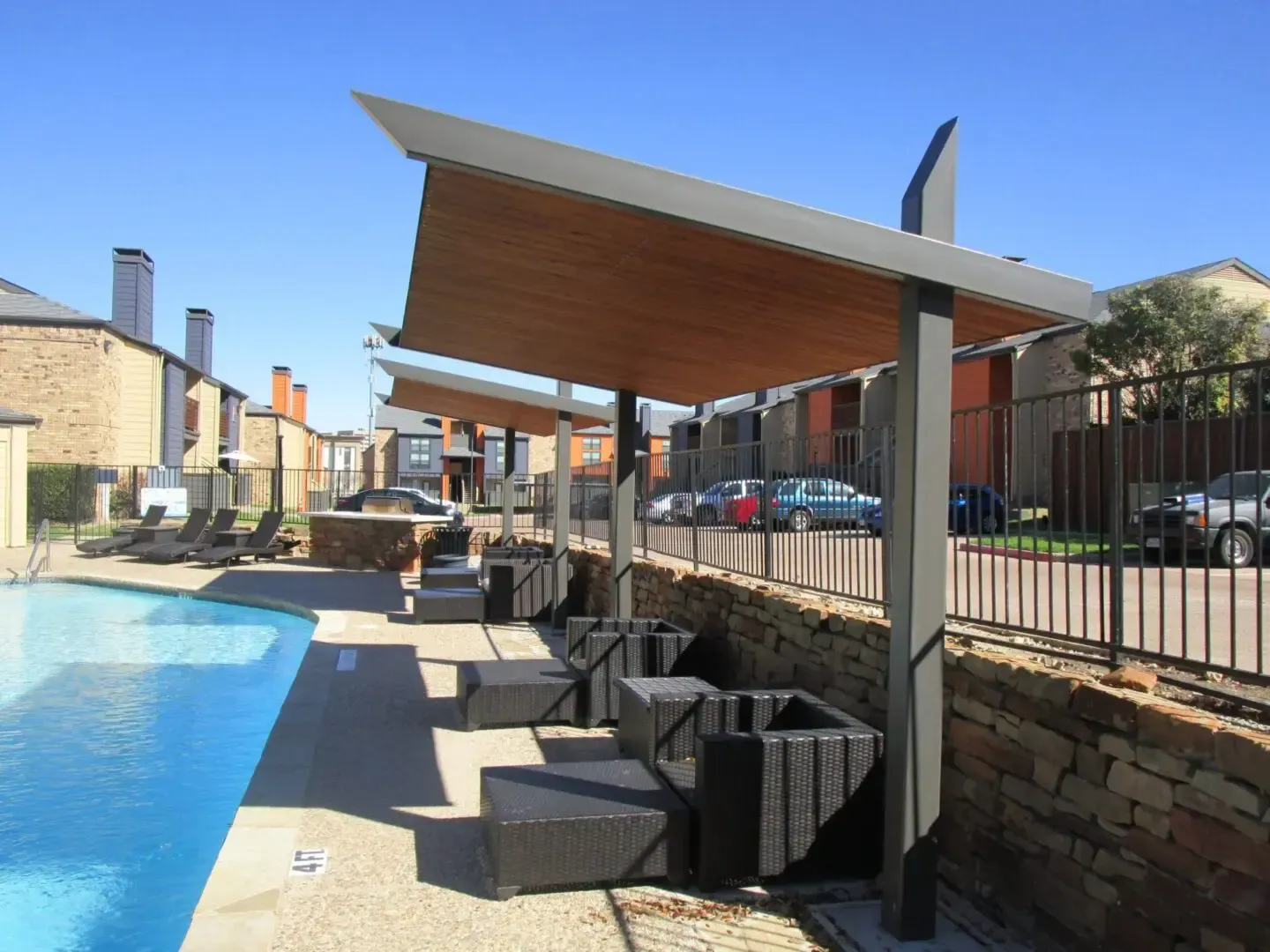 Poolside shaded seating with blue pool and brick wall.