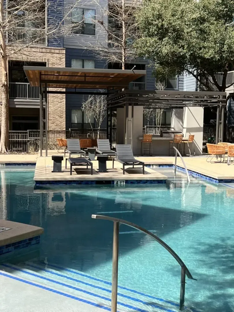 Pool area with chairs, gazebo, and bar. Apartment building in the background.