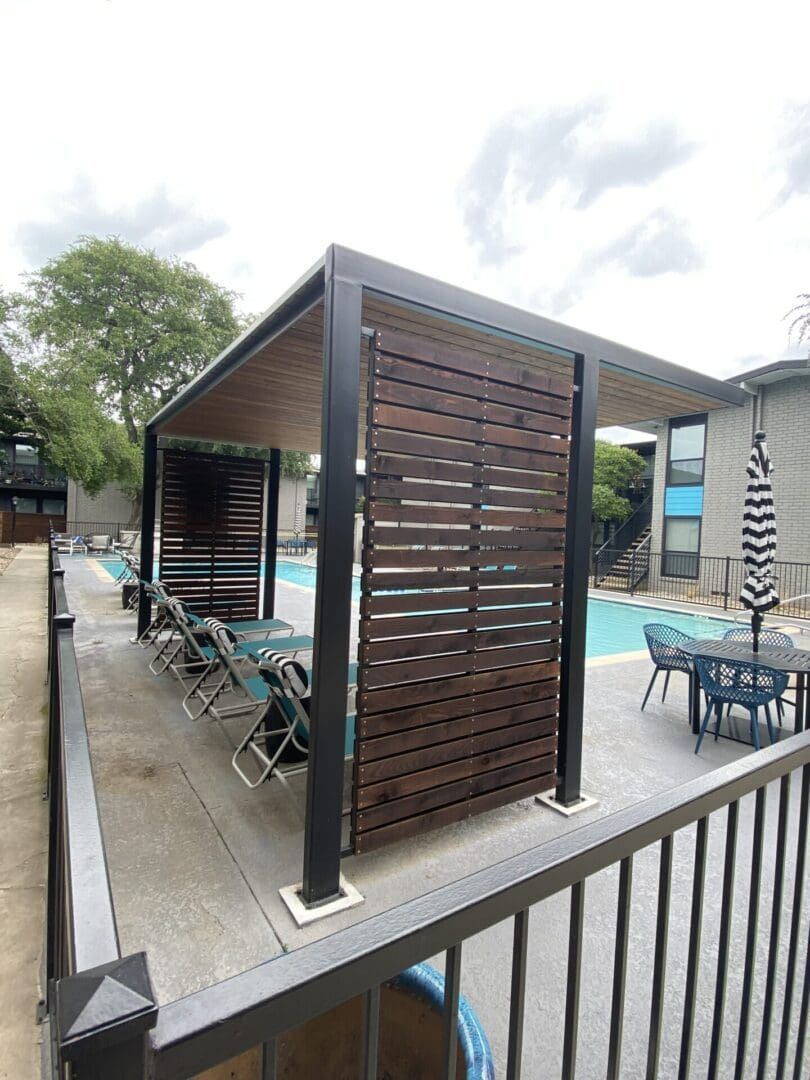 A poolside pergola with dark wooden slats, black frame, and tables/chairs.