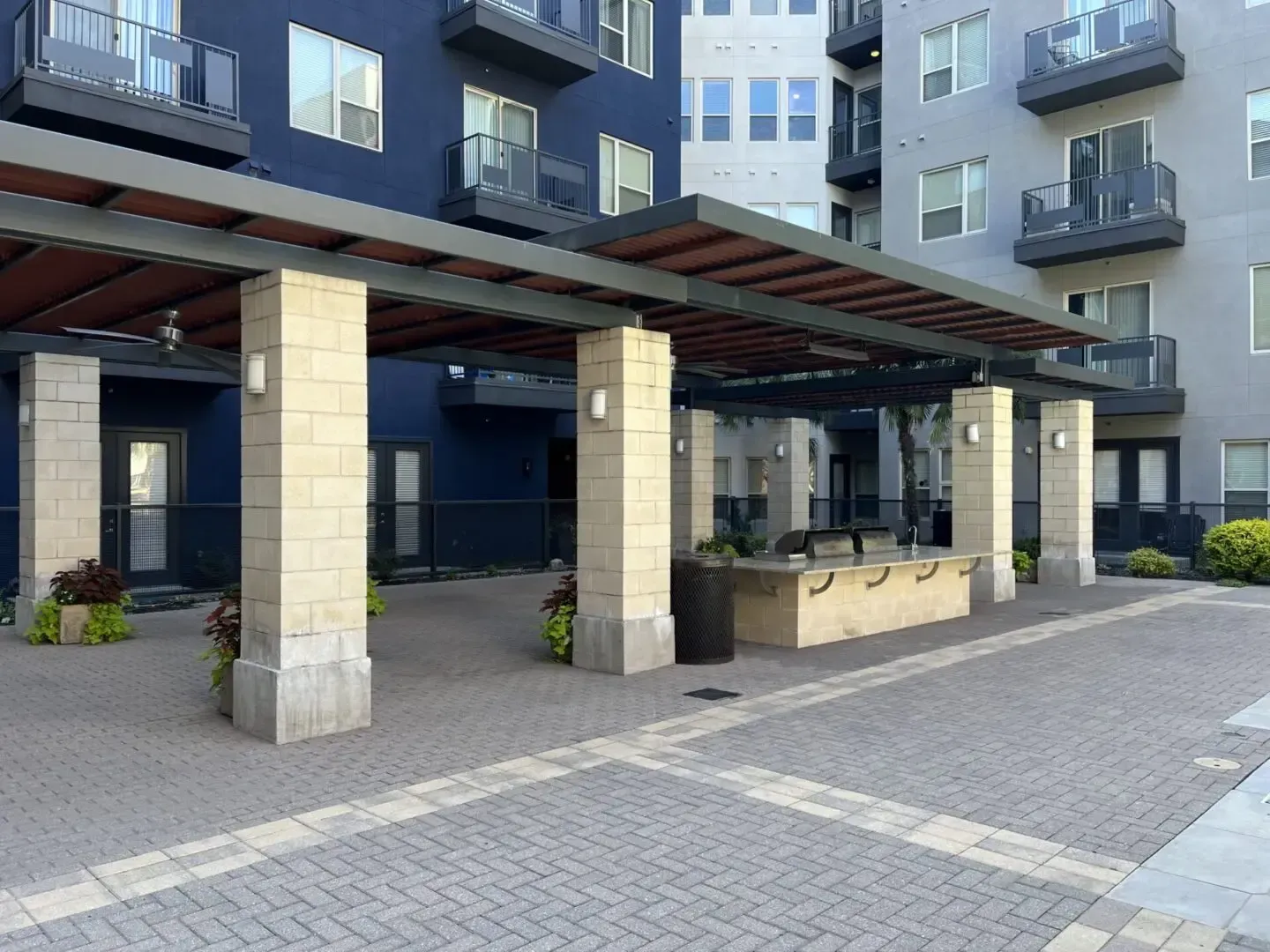 Outdoor patio with a pergola, stone pillars, and a brick paver floor in front of an apartment building.