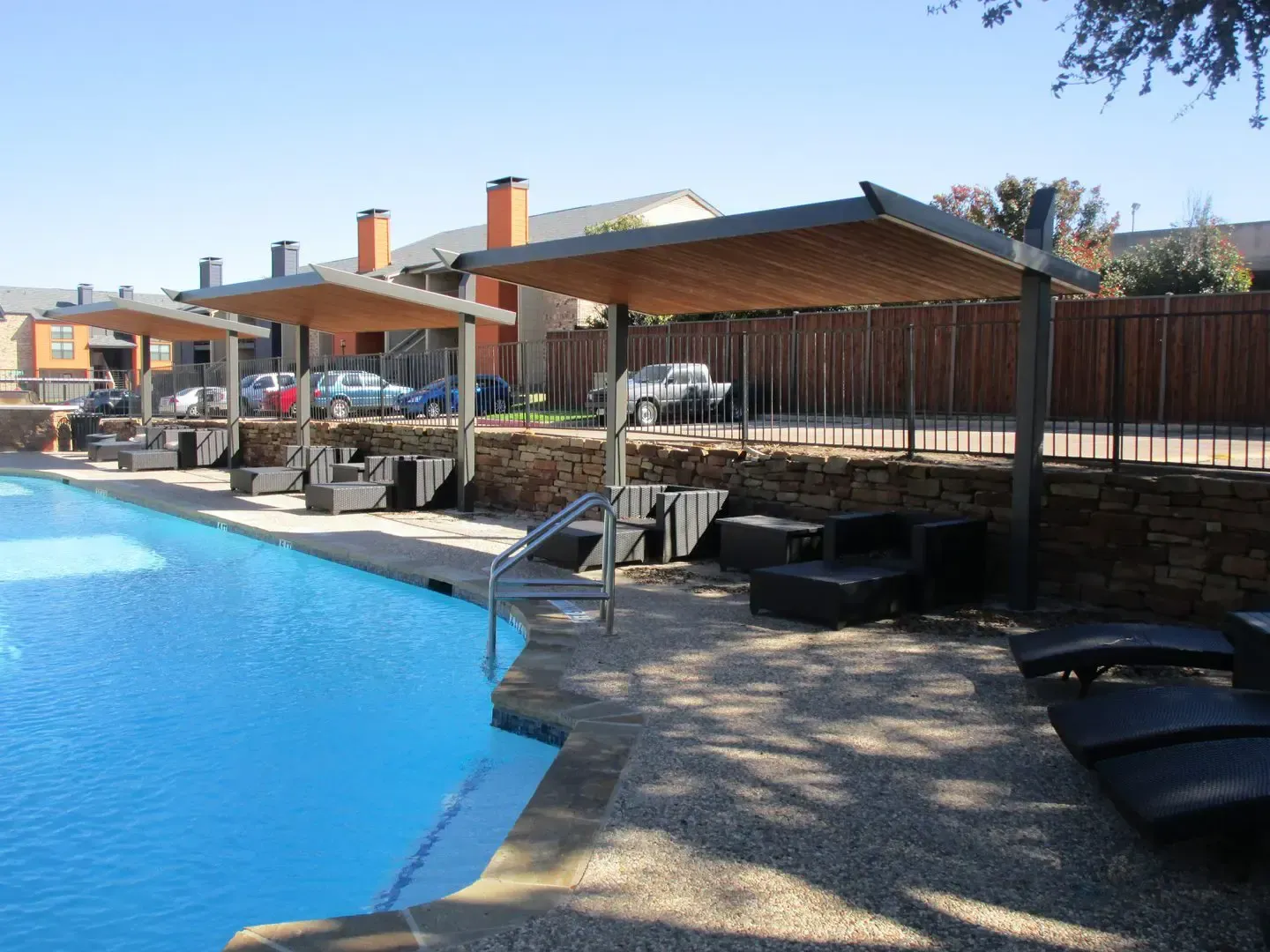 Poolside lounge area with canopies and chairs, blue water, brown stone, and a sunny sky.