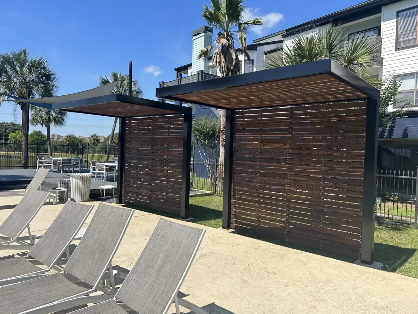 Two wooden cabanas near lounge chairs by a pool.