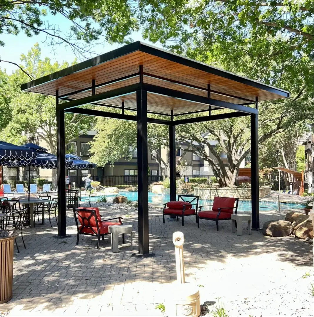 Gazebo with black posts, wood roof, red chairs, near pool.