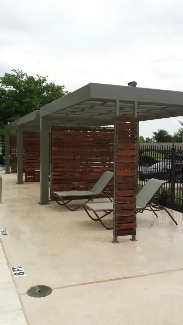 Poolside lounge area with shaded seating and two chairs under wooden panels.