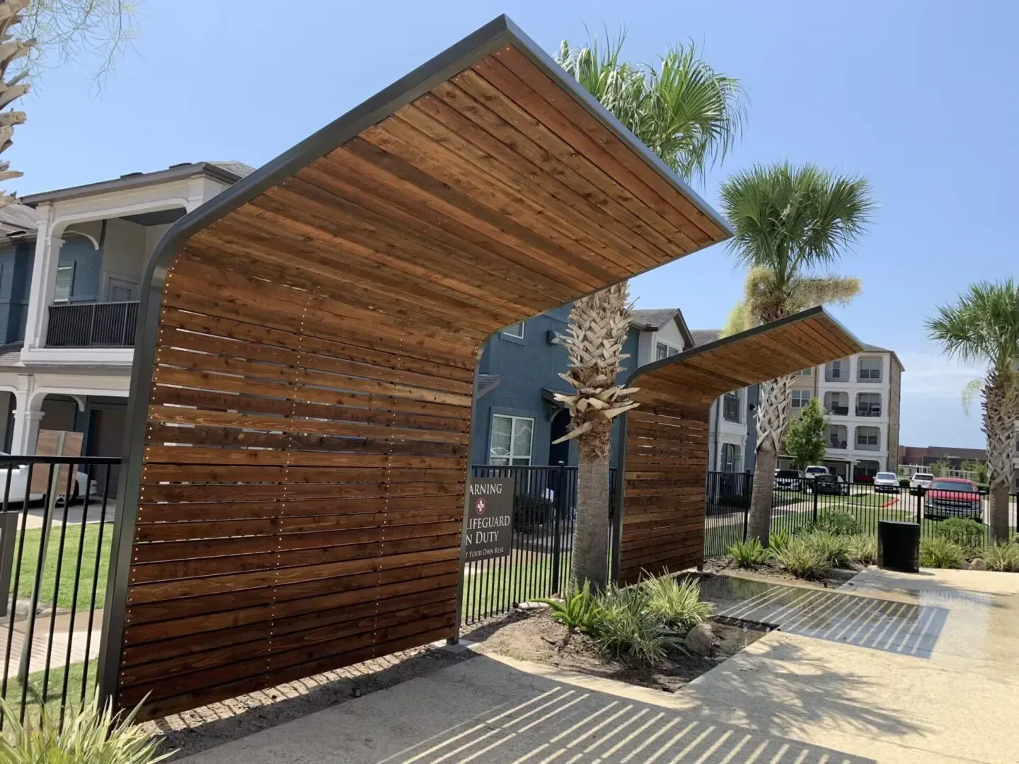 Wooden entryway with metal frame. Brown wood, blue building, palm trees. Sunny day.