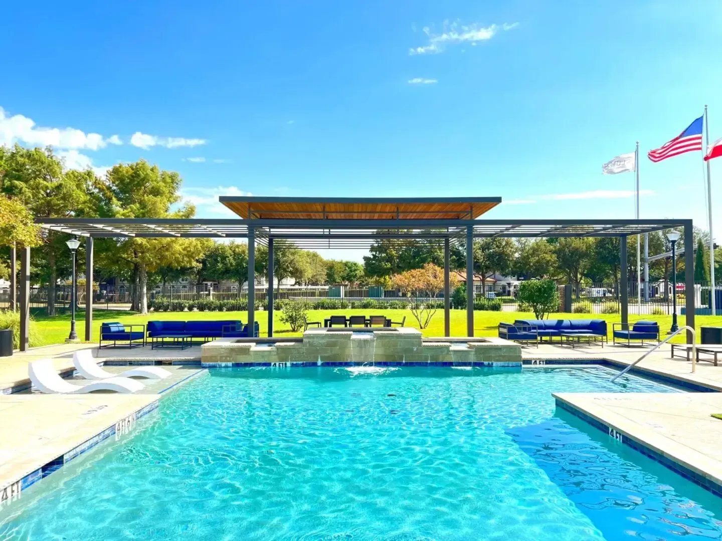 Swimming pool with a pergola, lounge furniture, and US flags on a sunny day.