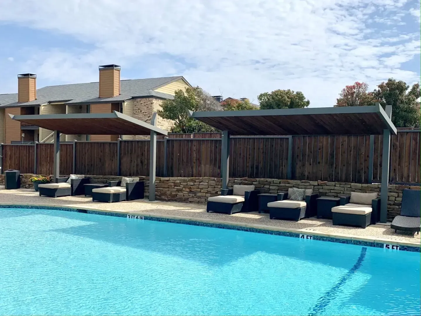 Poolside seating area: Lounge chairs under wooden shade structures next to a blue pool.