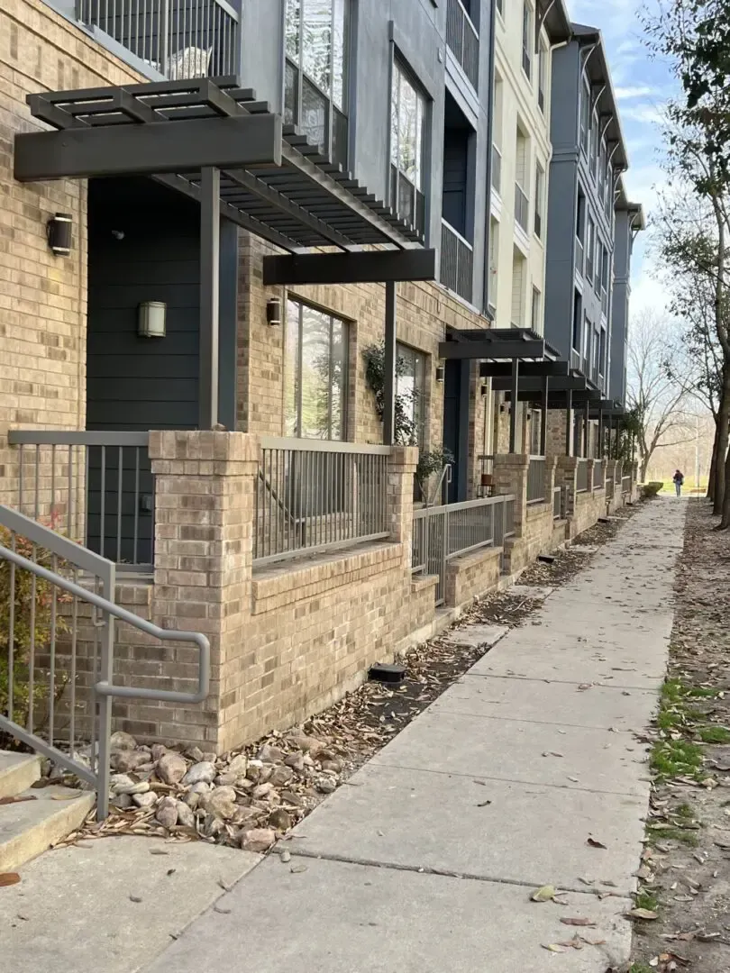 Brick building exterior with awnings, brick and metal railing, and a sidewalk; a person walks on the sidewalk.