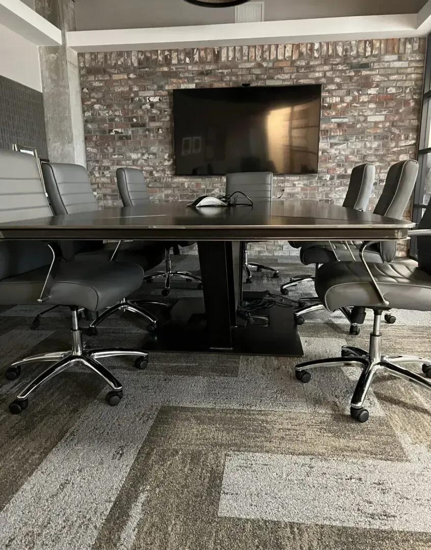 Conference room with large table, gray chairs, brick wall, and a TV.