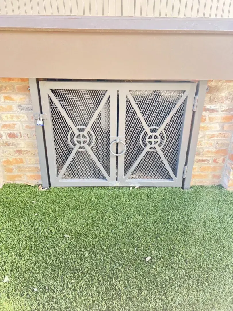 Gray metal cellar doors in a brick wall, set in a lawn with overhead awning.