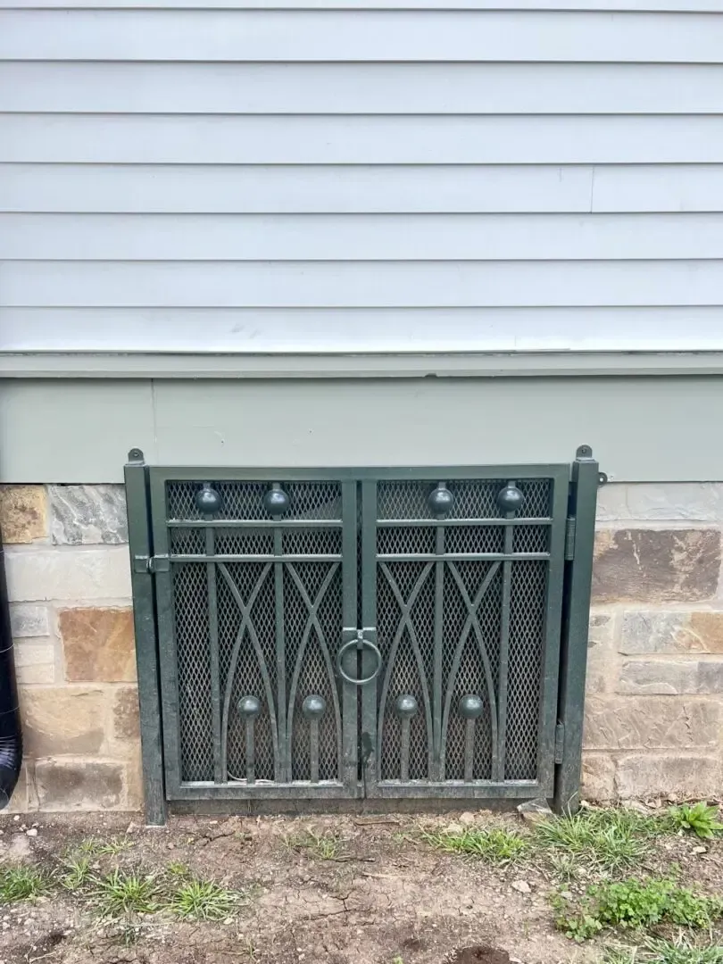 Green metal doors covering a basement window, against a stone and gray siding wall.