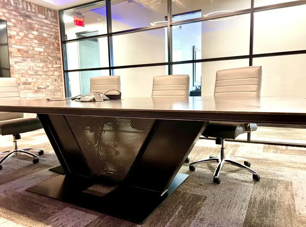 Modern conference room with large wood table, chairs, brick wall, and frosted glass windows.