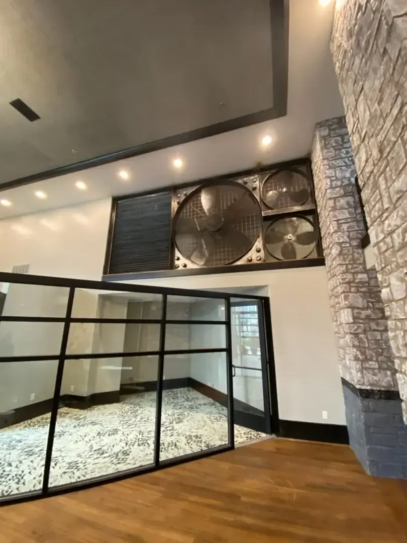 Large room with industrial fans, glass doors, and stone wall.