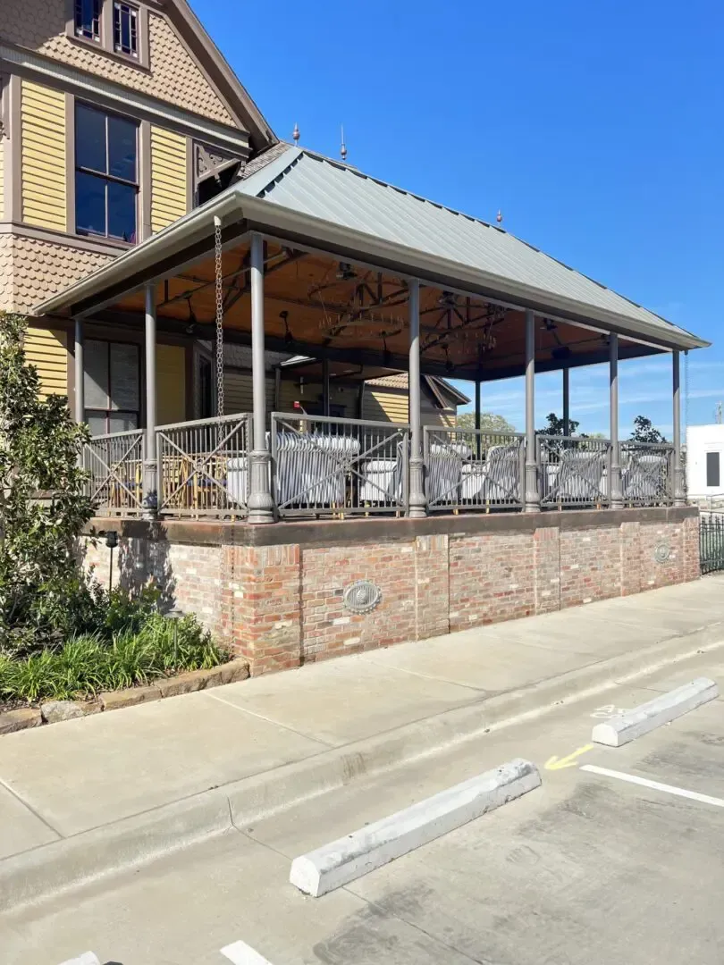 Covered patio with tables and chairs, brick base, metal roof, and sidewalk.