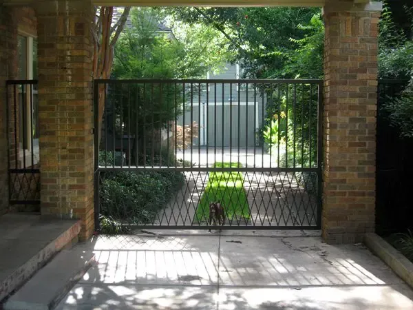 Black metal gate between brick columns; driveway leads to a green backyard.