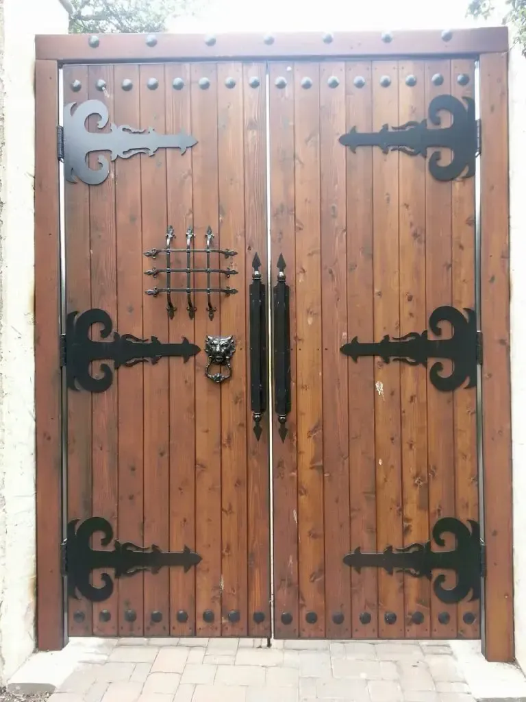 Wooden double doors with ornate black hinges, handle, and lion-head knocker.