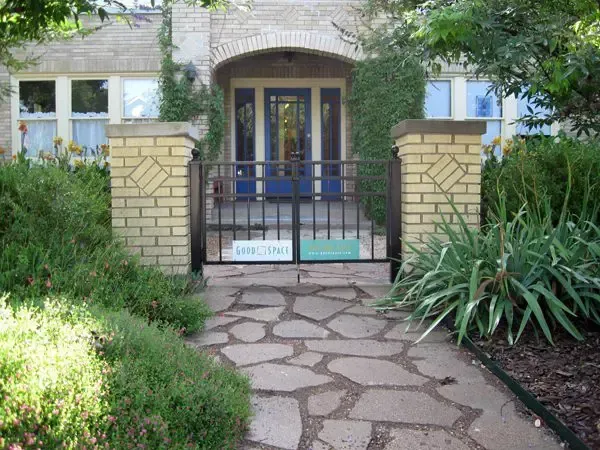 Stone path leads to a blue door with a wrought-iron gate; brick pillars frame the entrance.