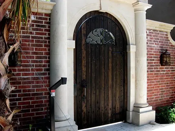 Wooden arched door with decorative window, framed by white columns and brick wall.