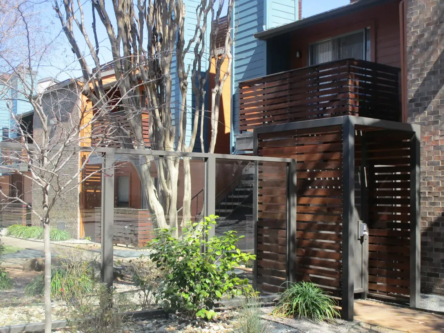 Apartment building with wooden slat design, trees, and shrubbery.