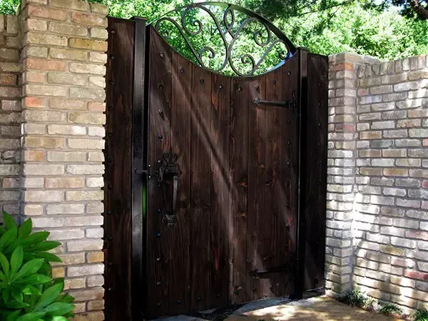 Wooden gate with decorative ironwork set in brick walls.