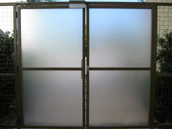 Two frosted-glass double doors in a dark metal frame, likely a gate in an outdoor setting.