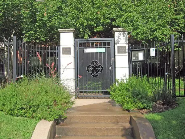 A gated entrance with a decorative iron gate, steps leading up, and greenery.